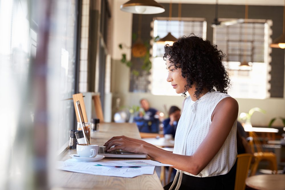 Businesswoman,By,Window,Working,On,Laptop,In,Coffee,Shop